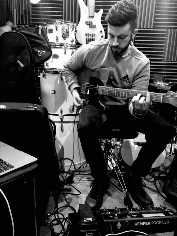 James playing guitar with studio equipment and drums behind him